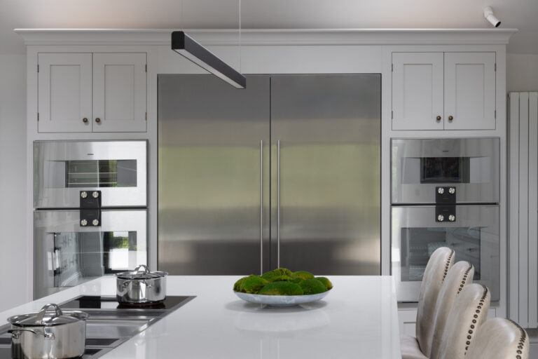 Kitchen island with induction hob and pans, facing a large stainless steel fridge freezer and built-in ovens
