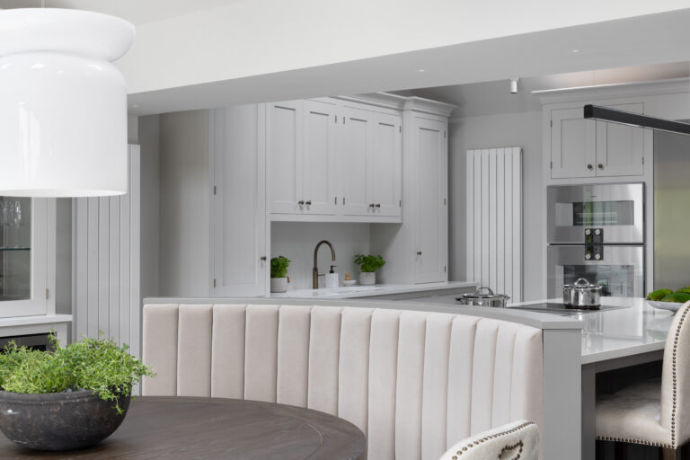 Curved banquette seating around the island, with painted cabinetry, brass tap and integrated oven beyond