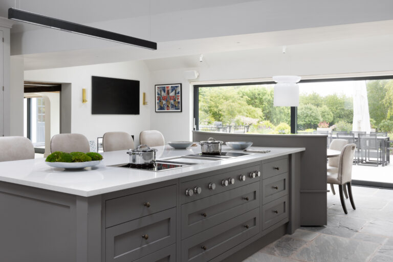 Large kitchen island with built-in hob and white worktop, opening onto a dining area with garden views