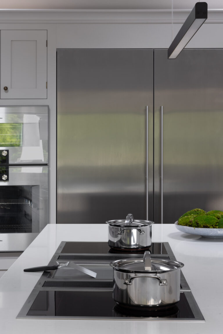 Kitchen island hob with stainless steel pans, built-in extractor vents and integrated fridge-freezer behind