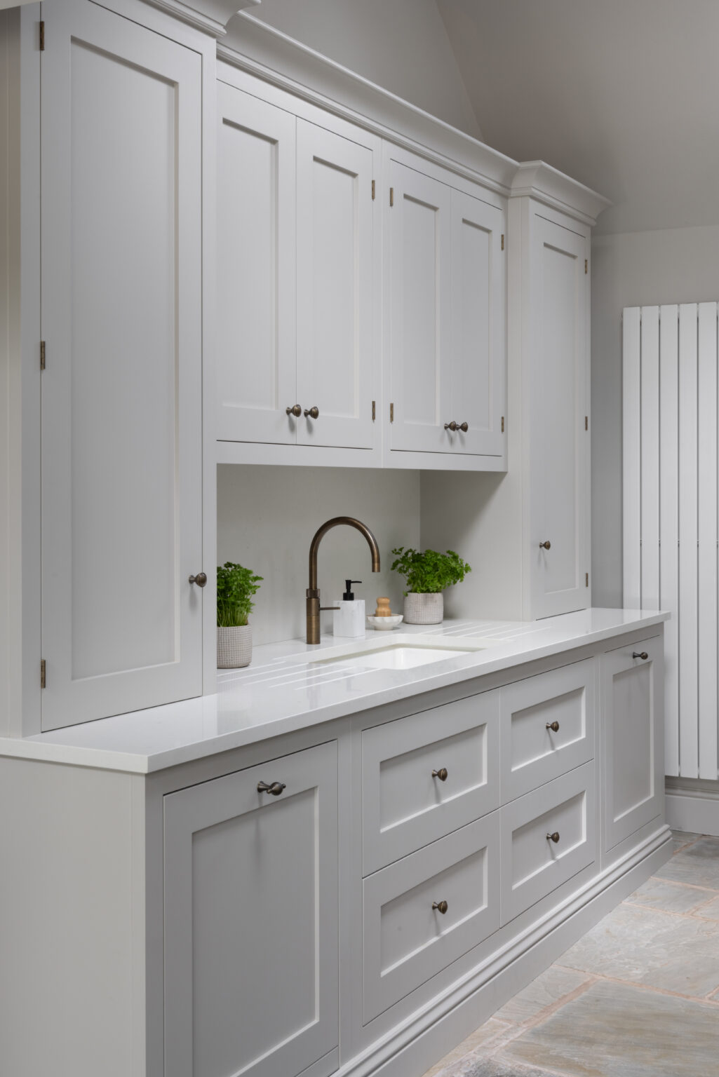 Laundry room run of shaker cabinetry with brass handles, inset sink and brass tap beneath wall cupboards
