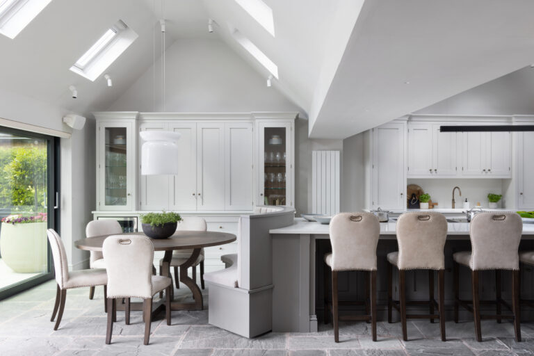 Vaulted kitchen with banquette seating built into the island, a dining table and glazed dresser beneath skylights