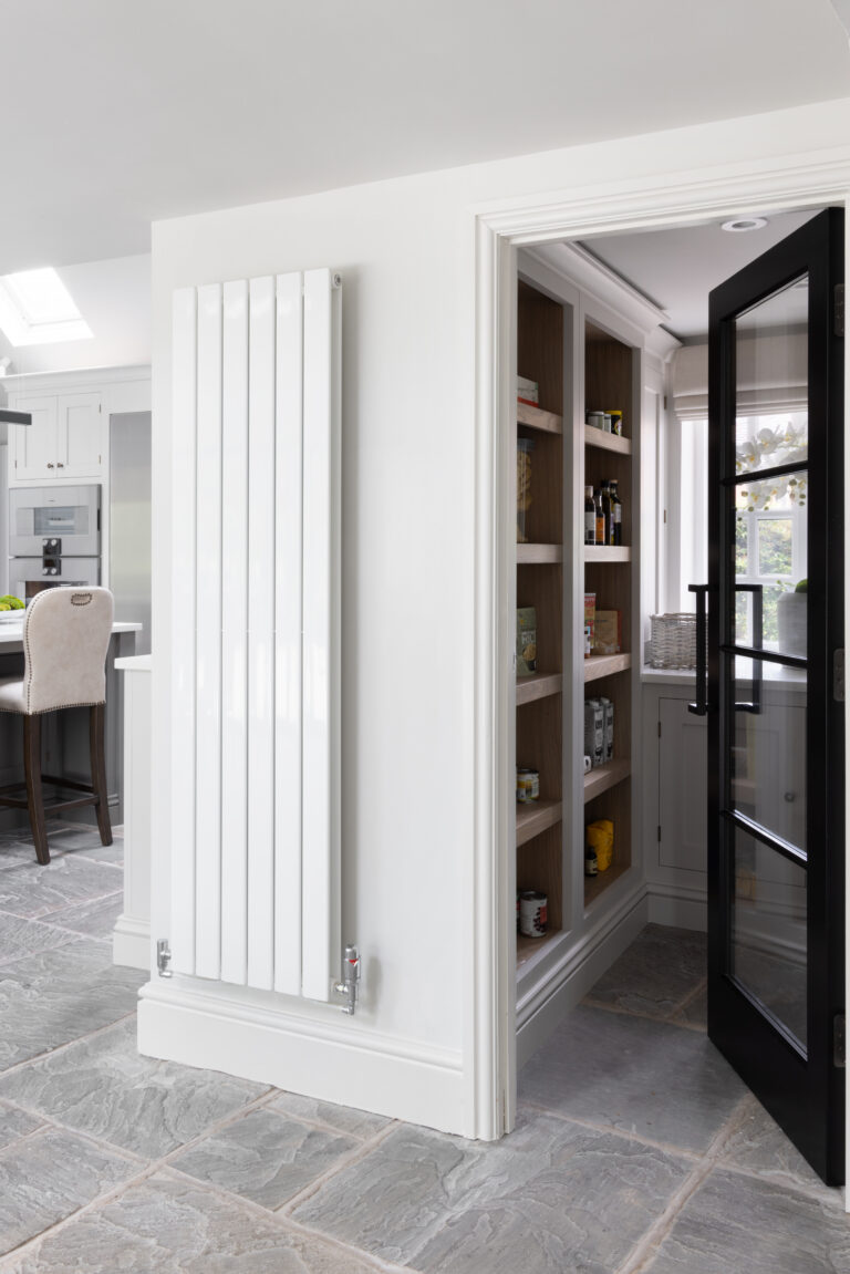 Walk-in pantry with open timber shelving, seen beyond a tall white radiator and black-framed glazed door