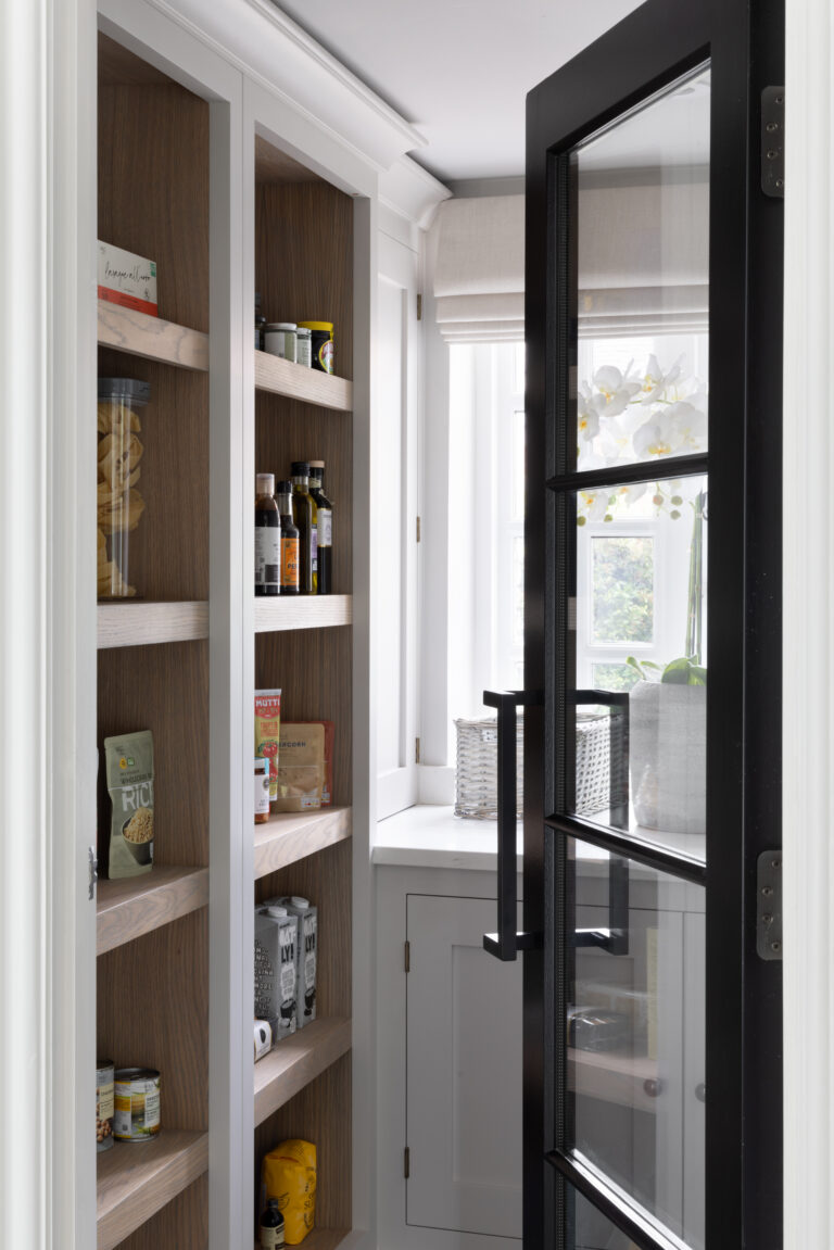 Walk-in pantry with open shelving, stocked food items, a crittall-style glazed door and bright windowsill beyond