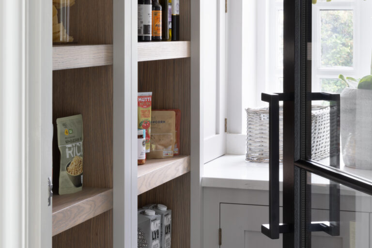 Walk-in pantry with shallow oak shelving behind glazed doors, storing jars, cartons and groceries