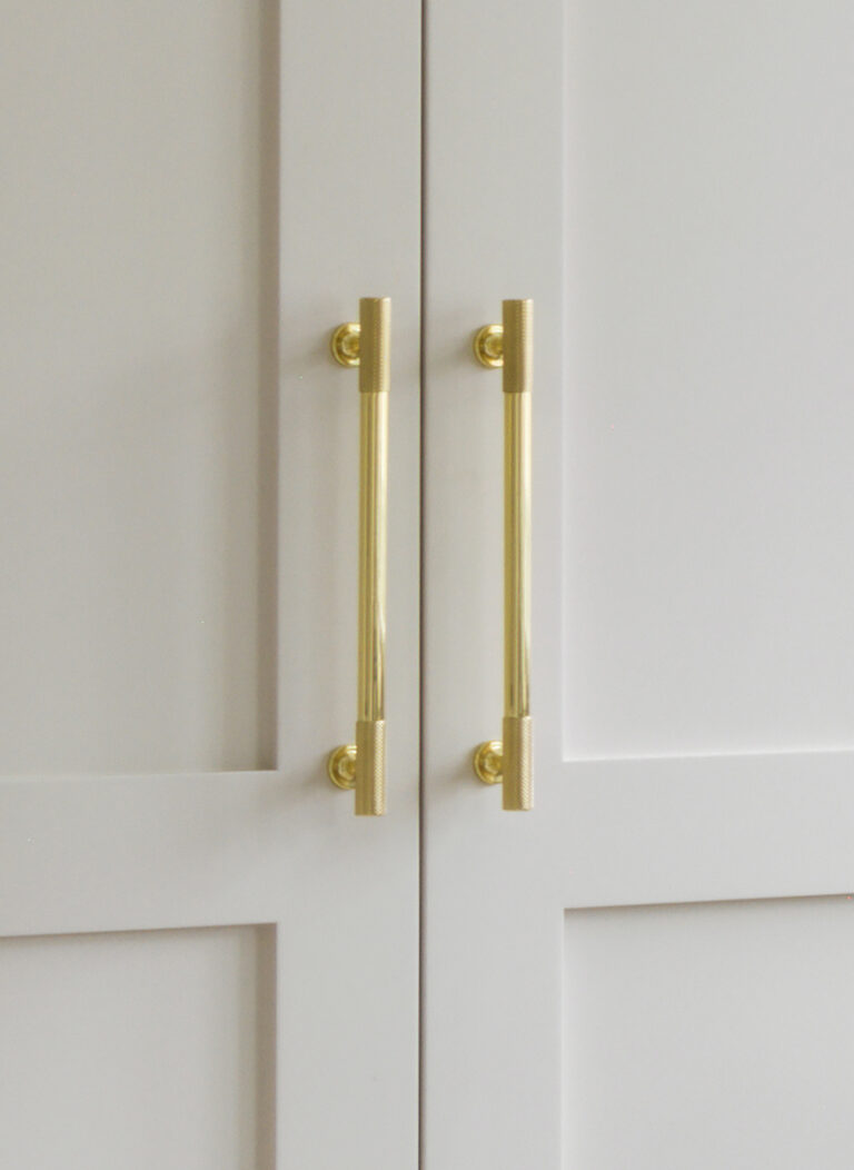 Close-up of shaker-style cupboard doors painted in Little Greene 'Joanna', fitted with brushed gold bar handles
