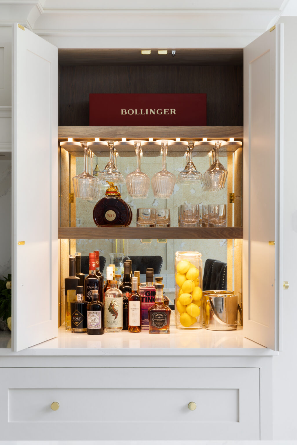 Open twin shaker-style doors reveal a stained oak interior home bar with glass racks, spirits, glassware and lit shelving