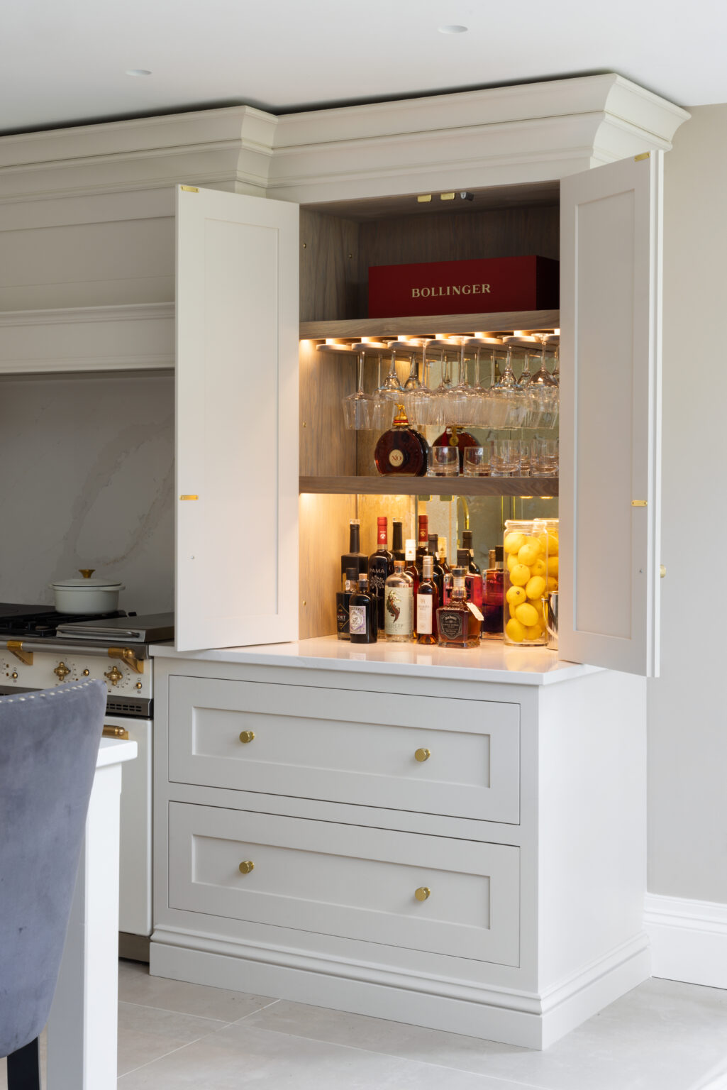 Shaker-style twin doors open to reveal a stained oak interior with glass racks, spirit bottles, and brass fittings