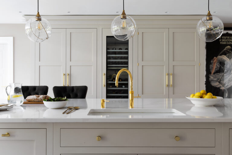 Kitchen island with brass tap and sink, built-in wine conditioner, glass pendant lights and panelled cabinetry behind