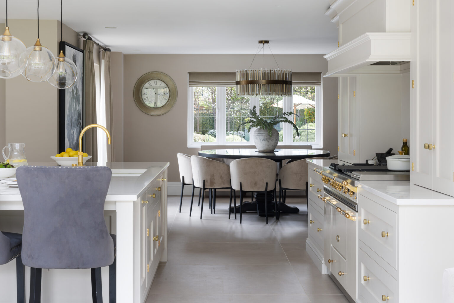 Open-plan kitchen with a Lacanche range cooker beside an island, leading to a round dining table and upholstered chairs