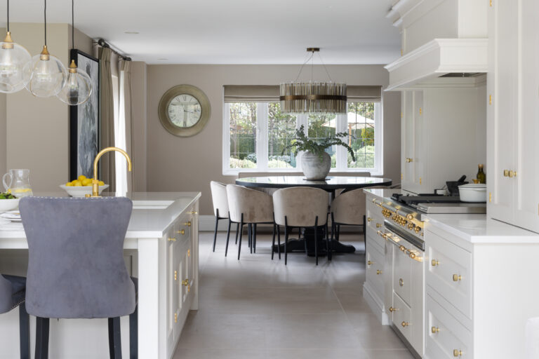 Open-plan kitchen with a Lacanche range cooker beside an island, leading to a round dining table and upholstered chairs