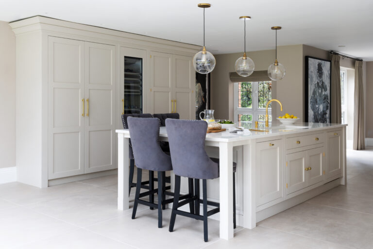 Open-plan kitchen island with bar stools, brass fittings, glass pendant lights and a built-in wine conditioner cabinet
