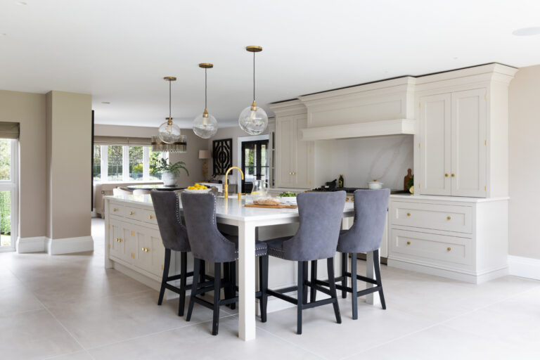 Open-plan kitchen with a large island bar, upholstered stools, brass fittings, and a range cooker beneath an extraction canopy