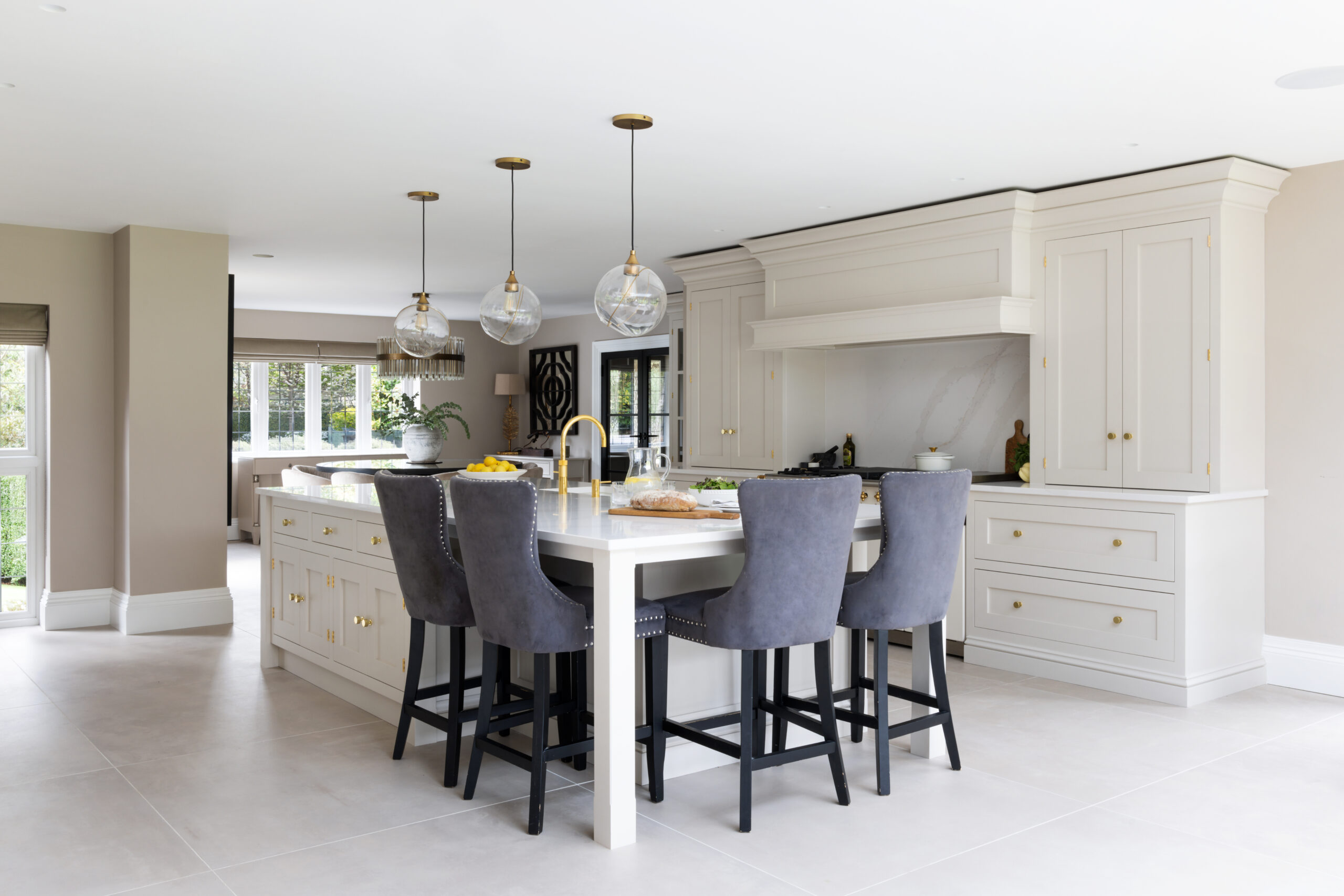 Open-plan kitchen island with grey upholstered stools, pendant lighting and a professional range set within panelled cabinetry