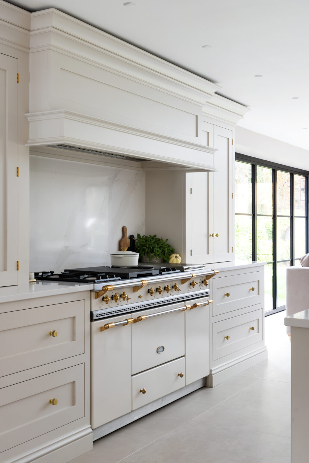 Lacanche range cooker with brass fittings set beneath a panelled extractor canopy and stone splashback
