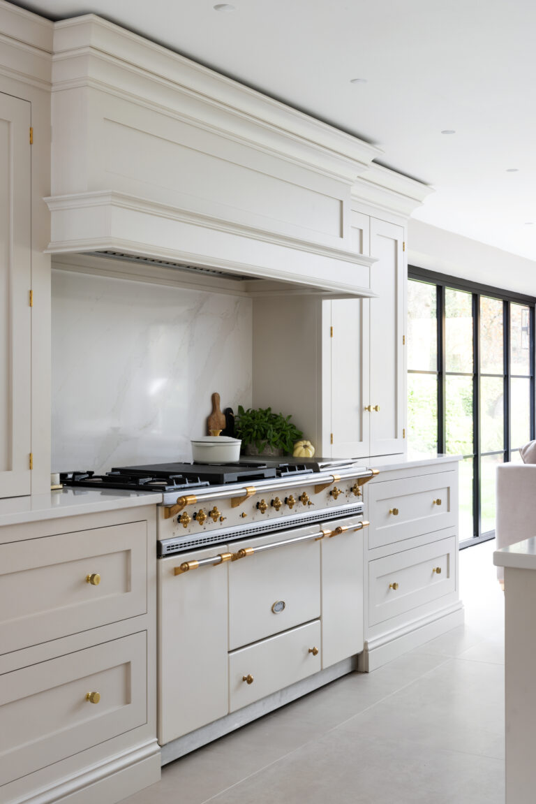 Lacanche range cooker with brass fittings set beneath a panelled extractor canopy and stone splashback