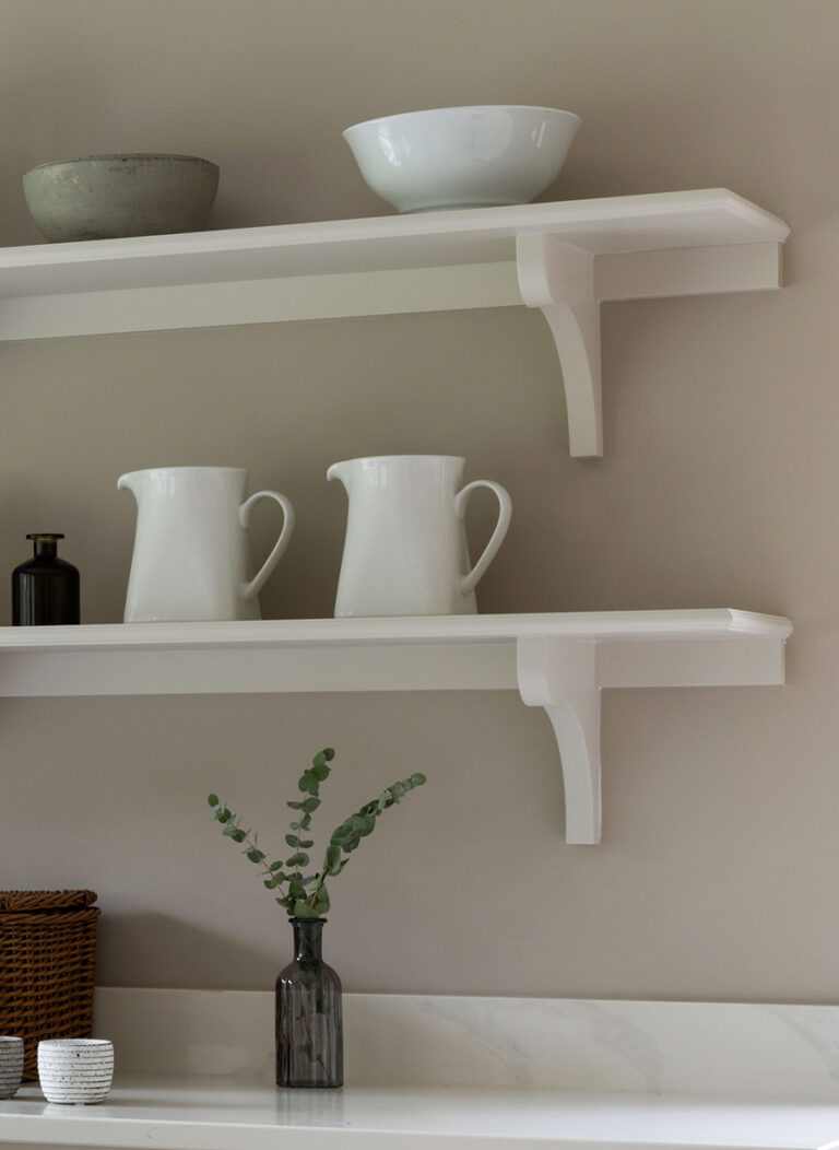 Open kitchen shelving with bracket supports, displaying ceramic jugs, bowls and a small glass vase with eucalyptus
