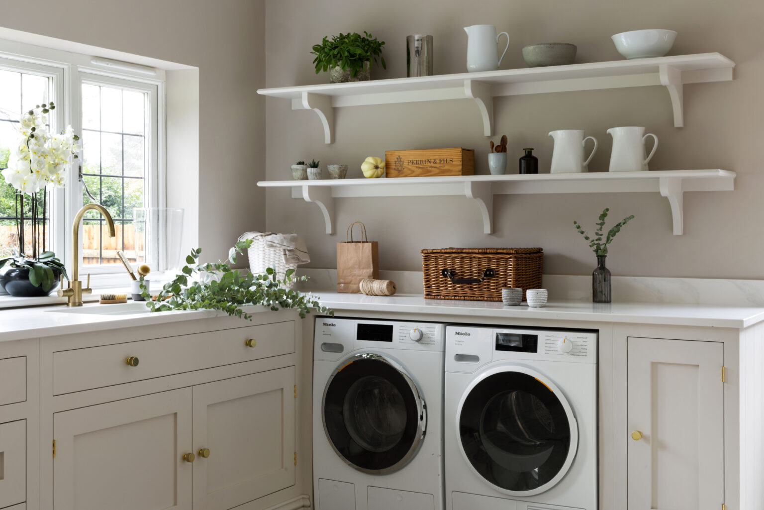 Utility room with fitted cabinetry, open shelving, integrated Miele washer and dryer, sink with brass tap and worktop