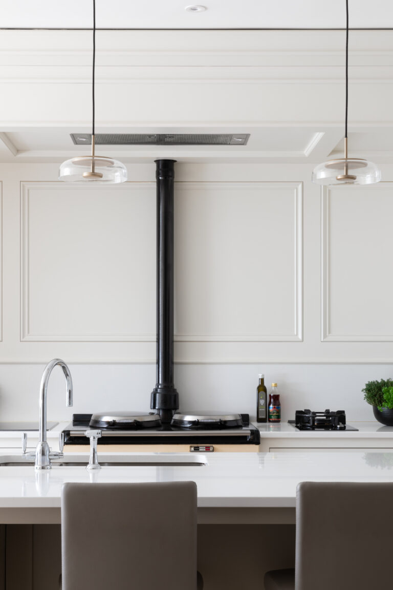 Kitchen with an Aga and black flue pipe, panelled walls, pendant lights and an island with upholstered stools