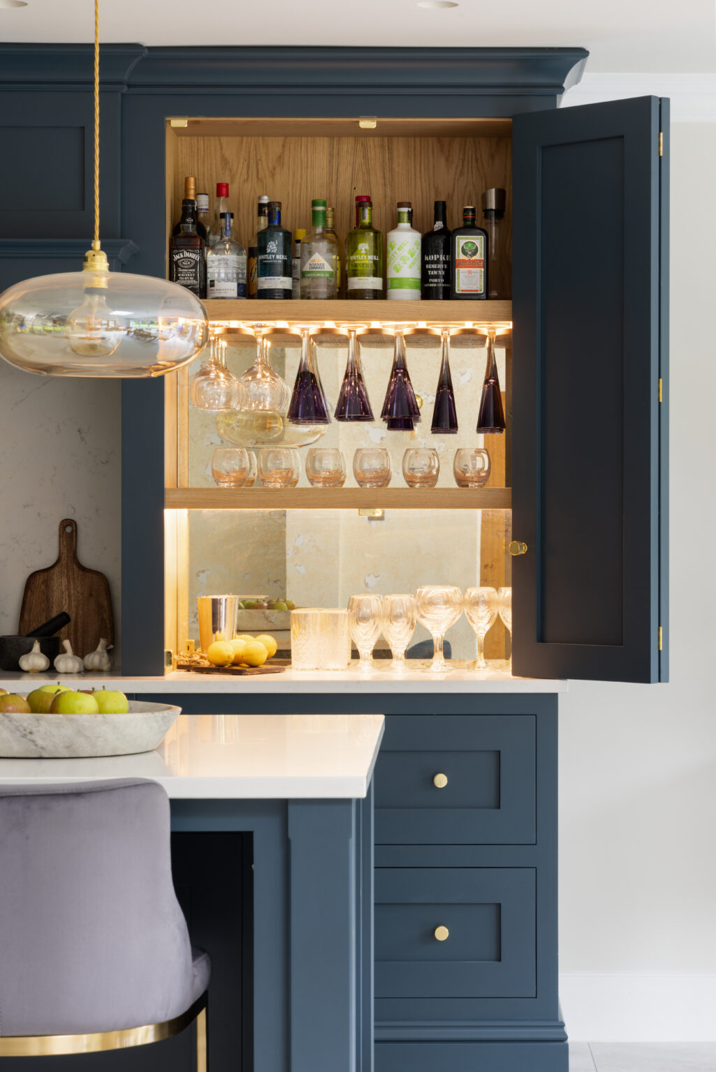 Open Farrow & Ball Hague Blue bi-fold cabinet revealing oak-lined bar with stemware racks and mirrored splashback