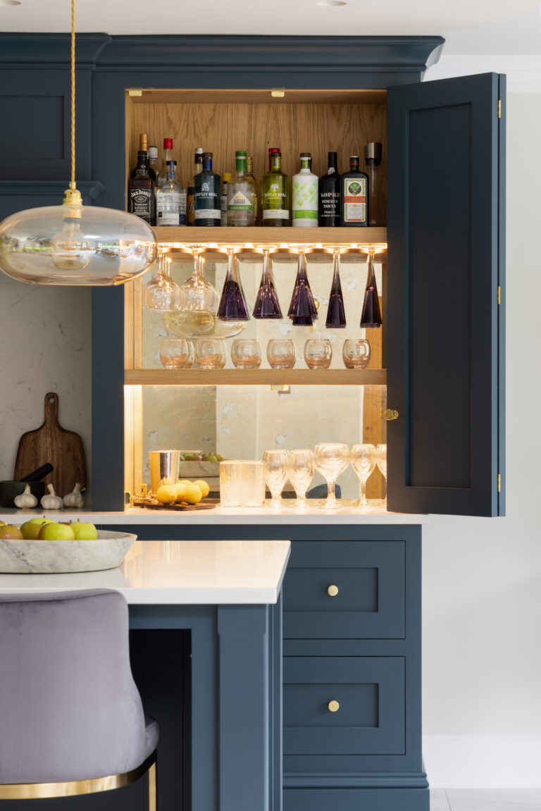 Open Farrow & Ball Hague Blue bi-fold cabinet revealing oak-lined bar with stemware racks and mirrored splashback