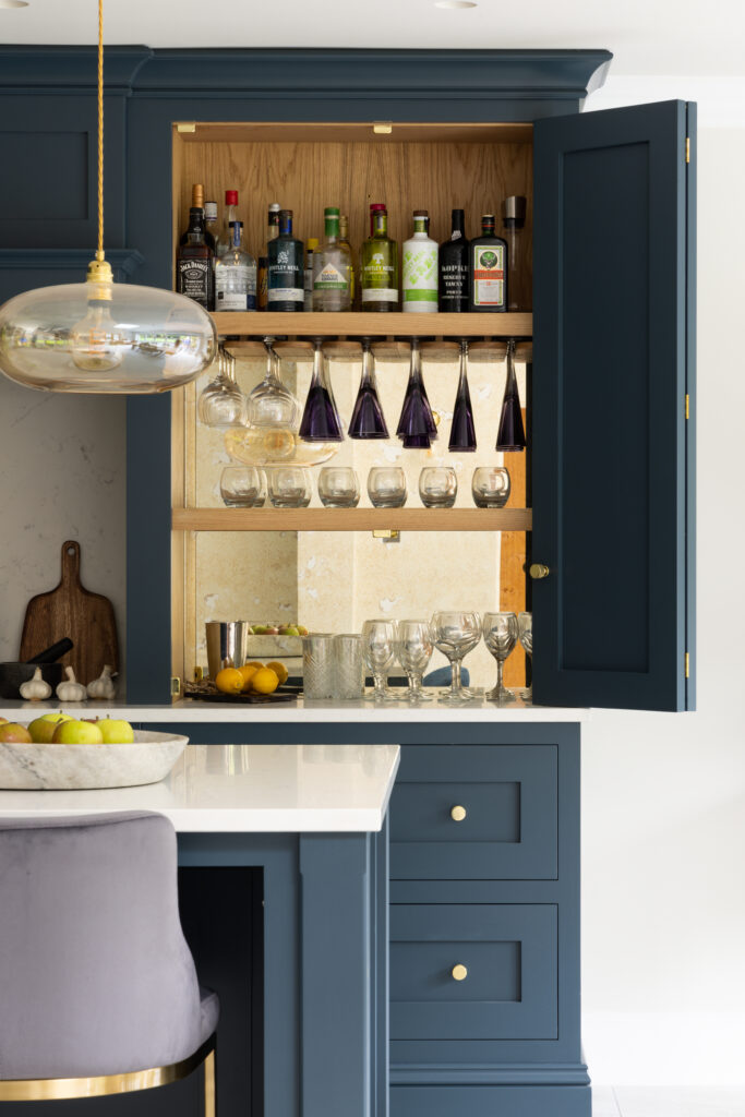Open Hague Blue bi-fold cabinet revealing an oak interior with stemware racks, spirit bottles and a mirrored splashback
