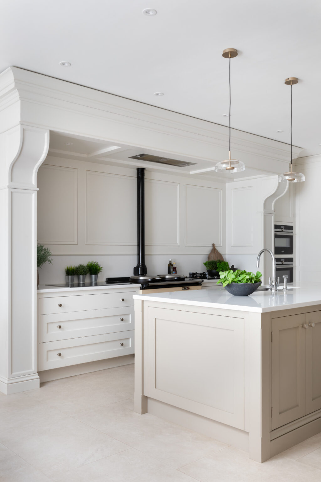White panelled kitchen with central island, pendant lights, and an Aga range beneath an arched recess