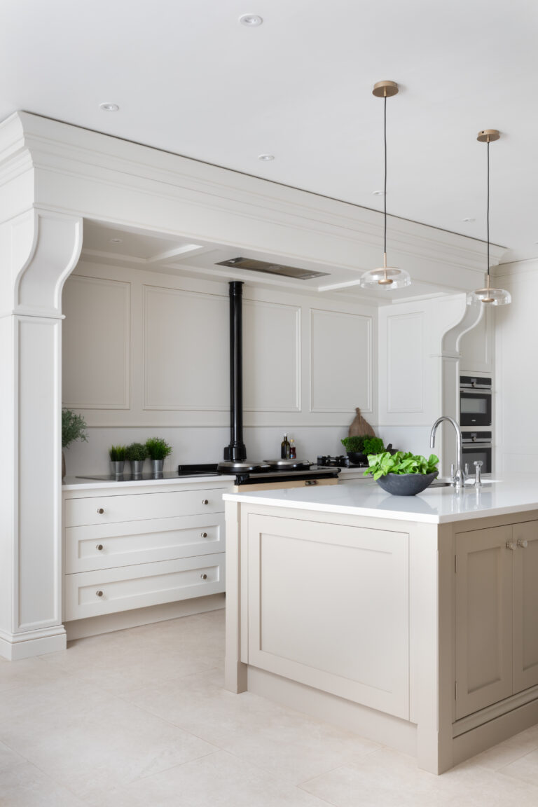 White panelled kitchen with central island, pendant lights, and an Aga range beneath an arched recess