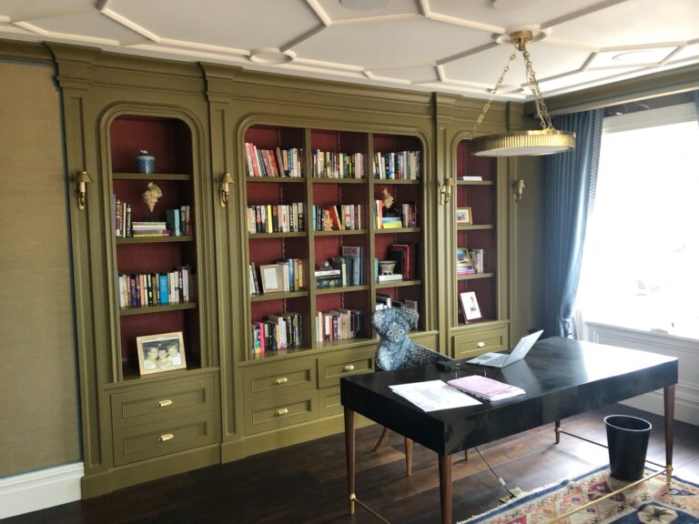 Study with fitted bookshelves, a dark desk with laptop and papers, and a patterned armchair by the window