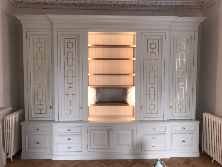 Large built-in cabinet with fretwork-panelled doors, brass handles, drawers below and an illuminated open shelving section