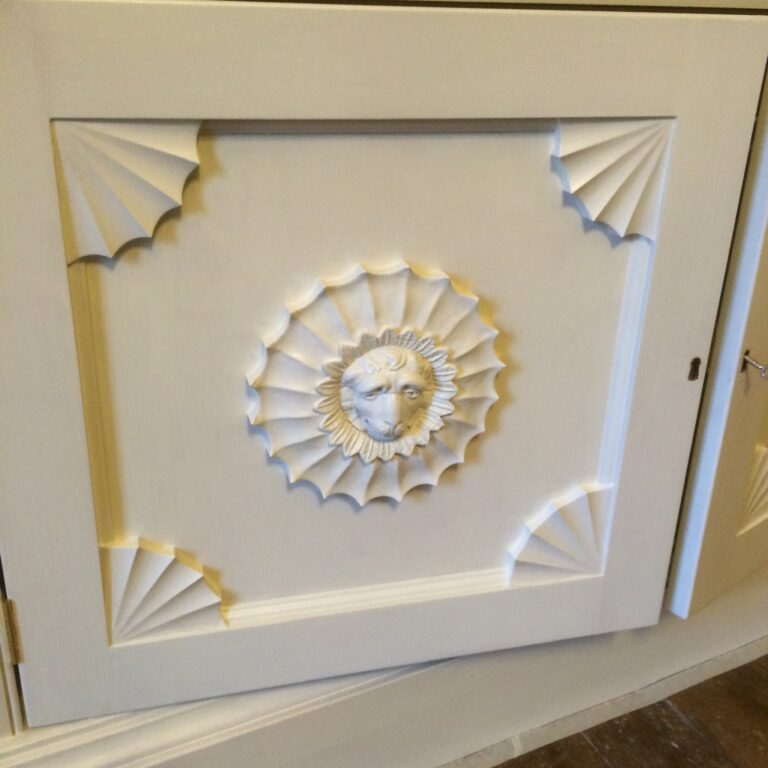 Painted cupboard door with carved fan corner details and a central lion's head rosette motif