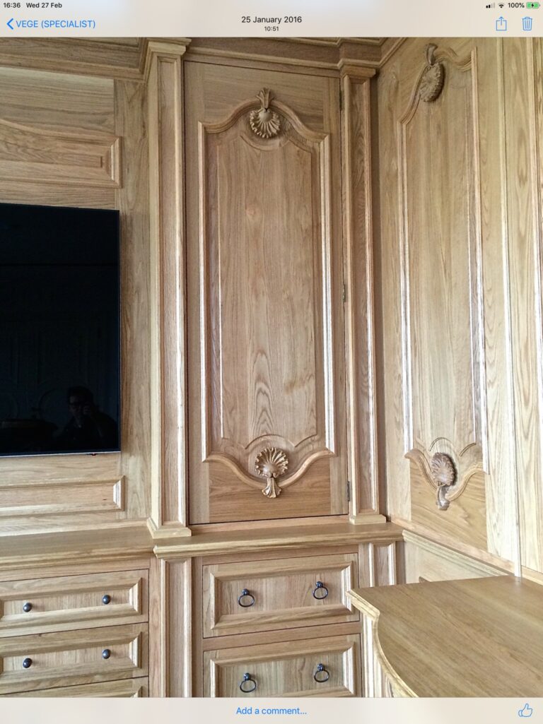 Bespoke panelled joinery with carved shell motifs, arched door, drawers with ring handles and an integrated television screen