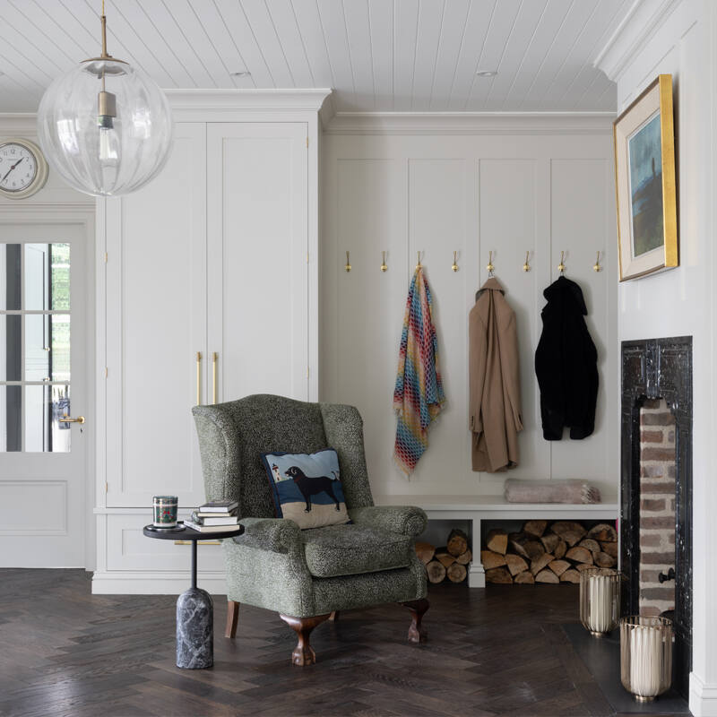 Boot room with herringbone timber floor, built-in cabinetry, Satin Brass hooks, wingback chair and open fireplace with log store