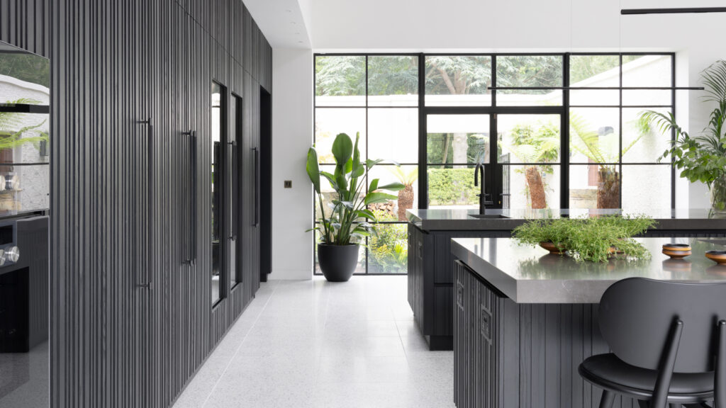 Kitchen with fluted dark cabinetry, a long island with grey worktop, and large glazed doors onto the garden