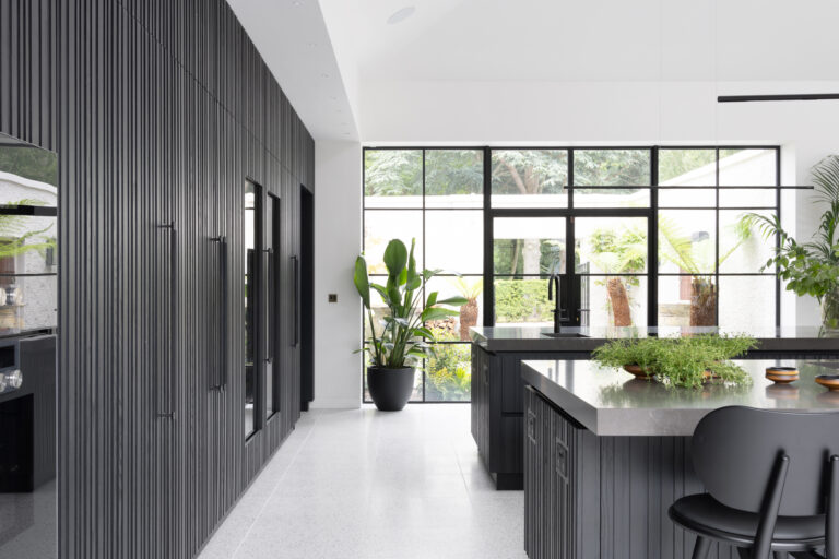 Open-plan kitchen with fluted black cabinetry, a large island unit and full-height steel-framed windows overlooking greenery