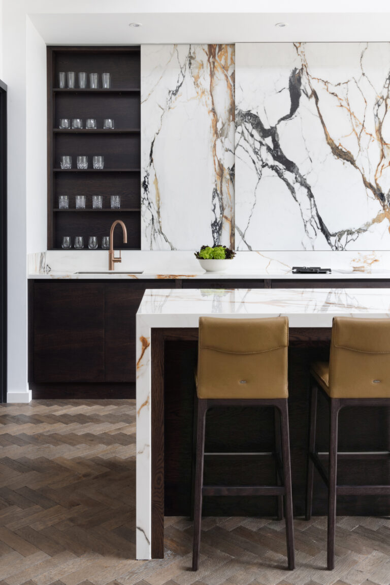 Kitchen island with a moving stone wall, dark cabinetry, open glassware shelving and tan leather bar stools