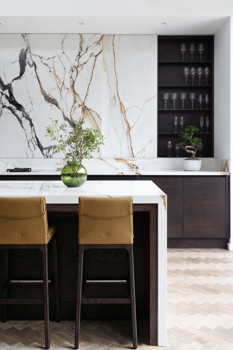 Kitchen island with mustard bar stools, a moving stone wall, and open shelving displaying glassware