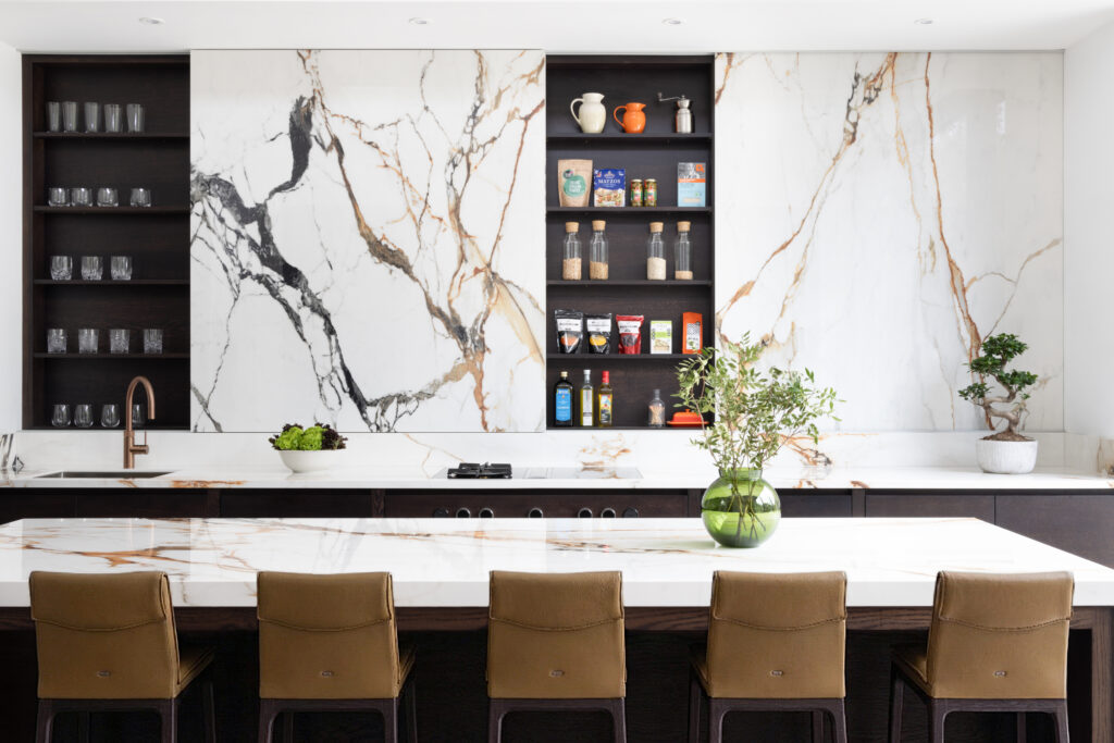 Kitchen island with a moving stone wall, open shelving, bar stools and a stone worktop