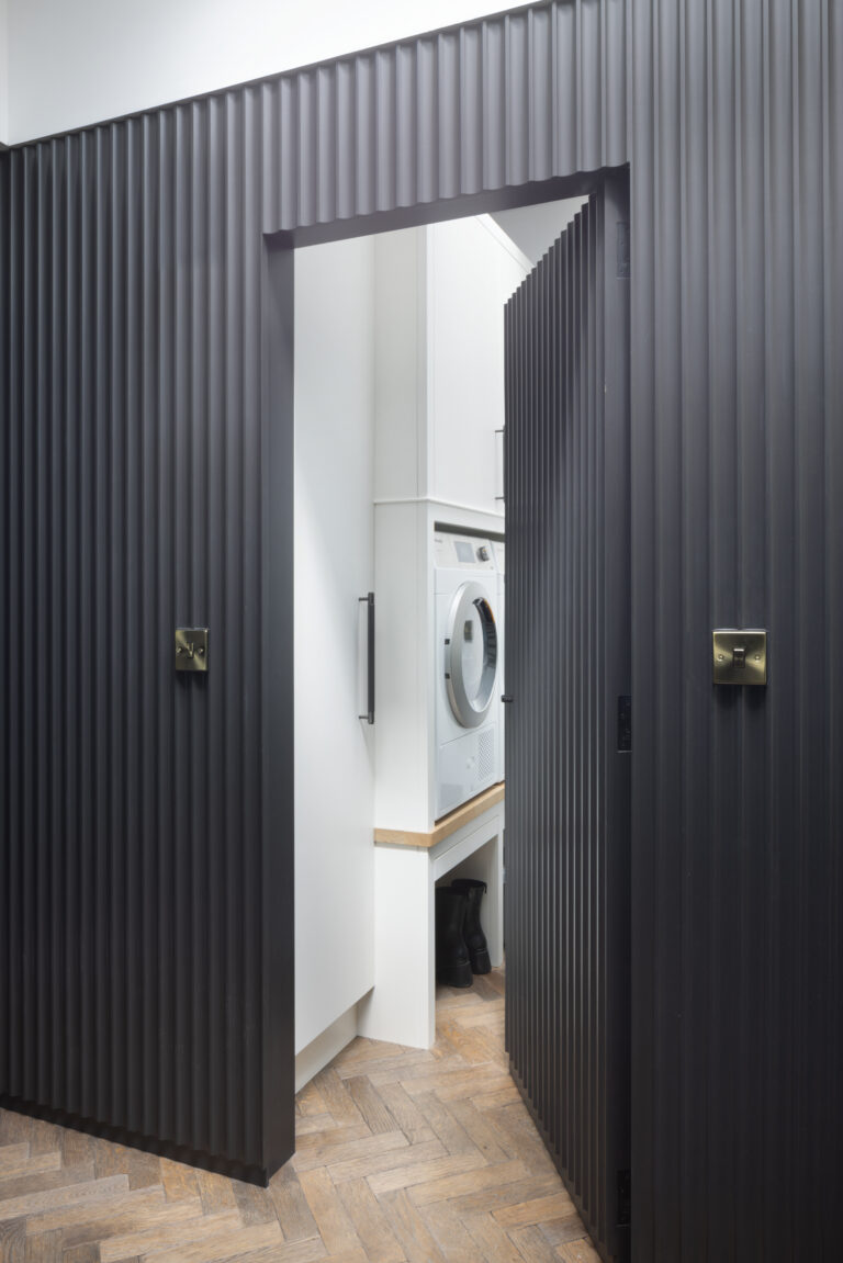 Fluted panelled door opens onto a laundry room with built-in washer-dryer and herringbone parquet flooring