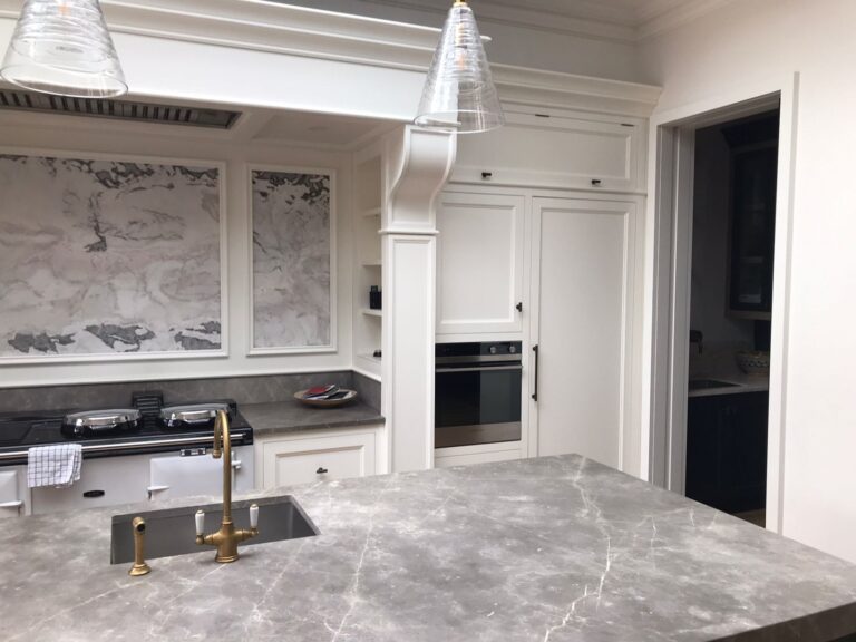 Bespoke kitchen with island sink, brass tap, built-in oven, range cooker and grey stone worktops and splashback panels