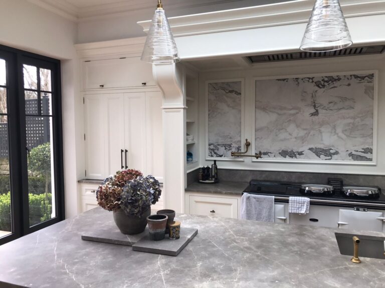 Kitchen with cream cabinetry, stone splashback panels, a stone island and a range cooker with brass tap fittings