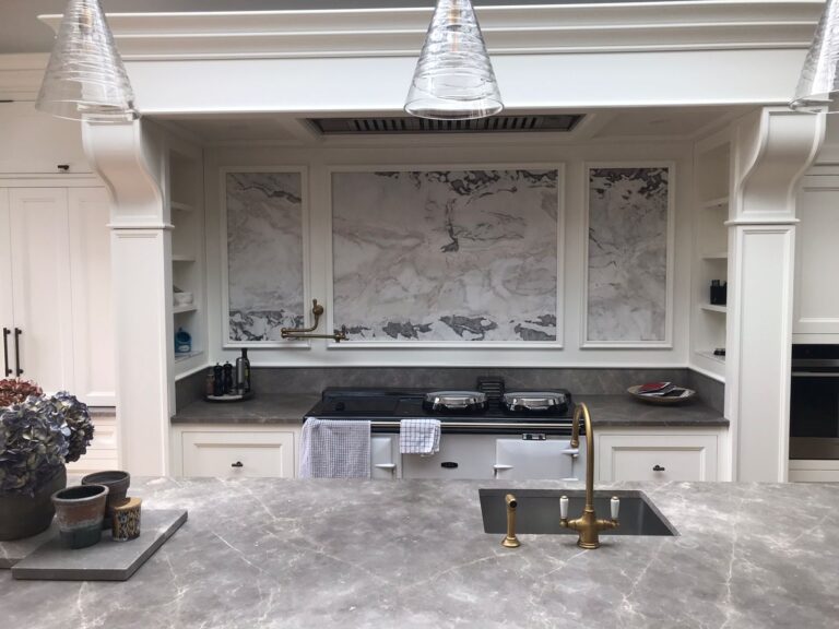 Bespoke kitchen with cream cabinetry, stone splashback panels, a range cooker and brass taps over a stone worktop