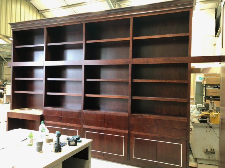 Large bespoke bookcase with open shelving above and panelled cupboards below, standing in the joinery workshop