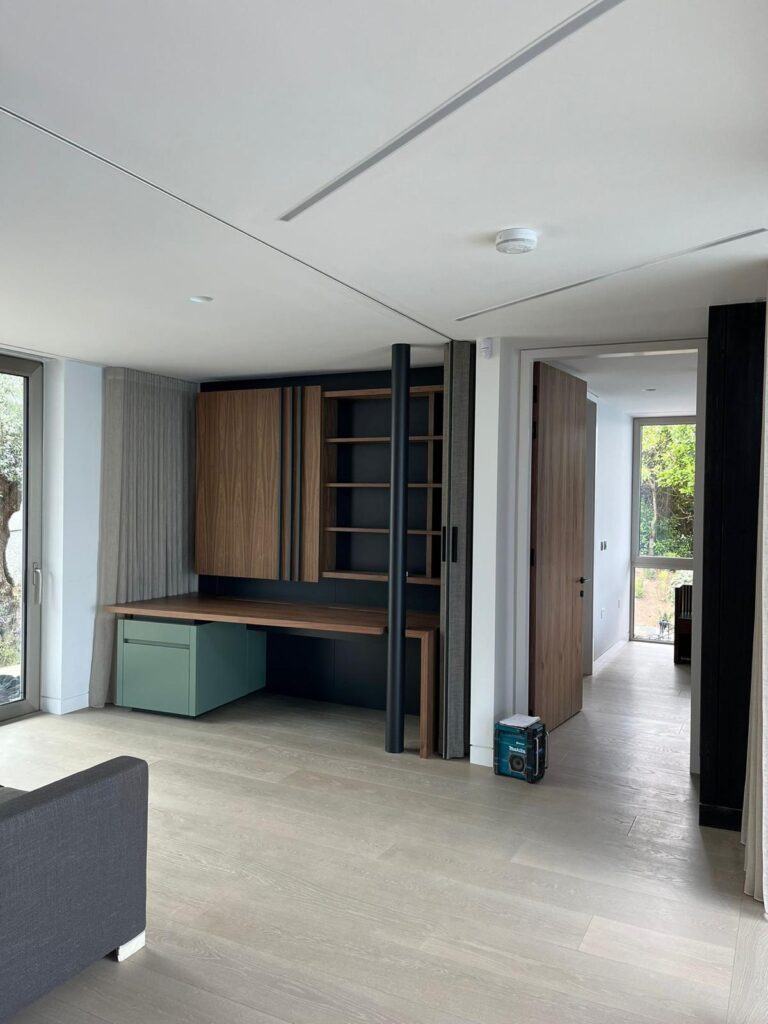 Living area with a built-in timber desk, open shelving, panelled cupboards and a green storage drawer unit beneath