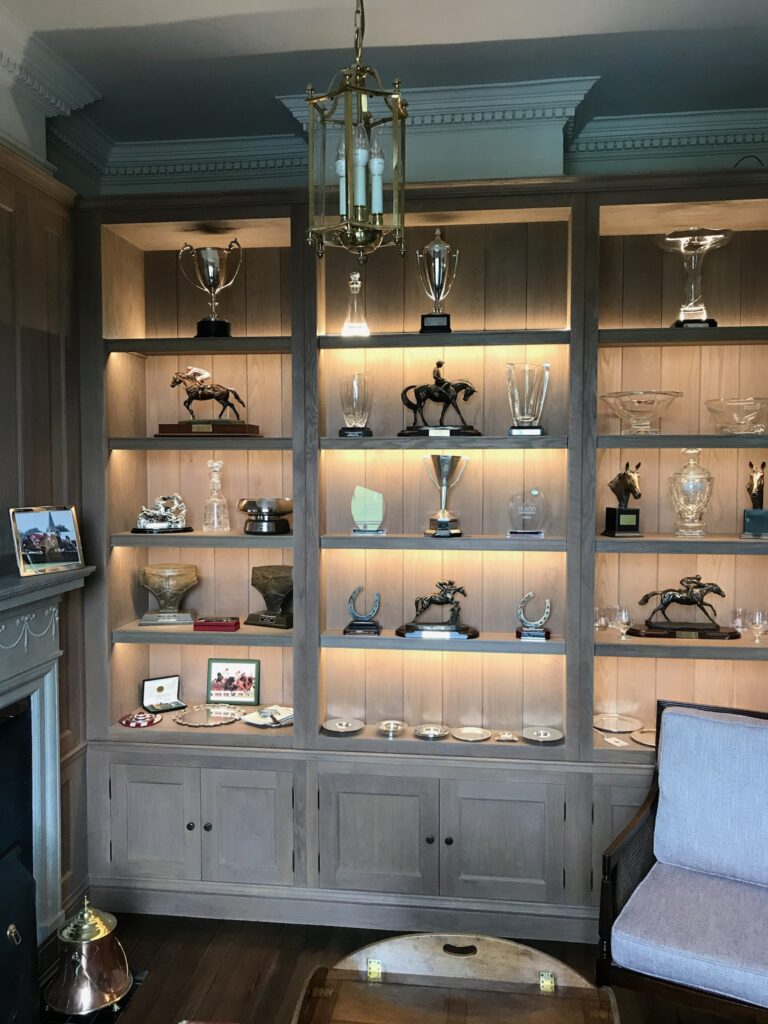 Fitted shelving unit with cupboards below, displaying racing trophies and ornaments under lit alcoves with a hanging lantern