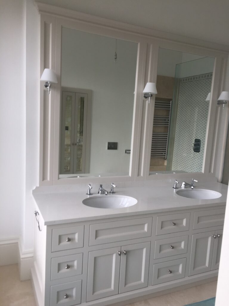 Bathroom vanity unit with twin inset basins, panelled cabinetry, tall mirrors and chrome wall lights above