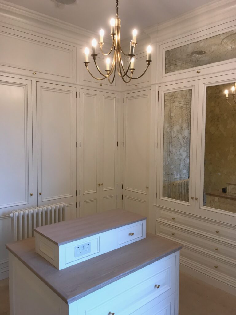 Dressing room with fitted wardrobes, mirrored doors, a central island unit and a brass candle-style chandelier
