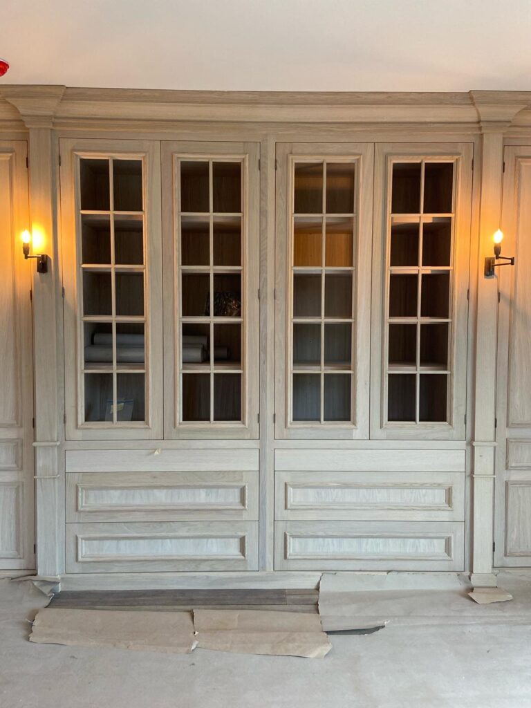 Built-in display cabinet with glazed doors, panelled drawers and wall lights either side, shown mid-installation