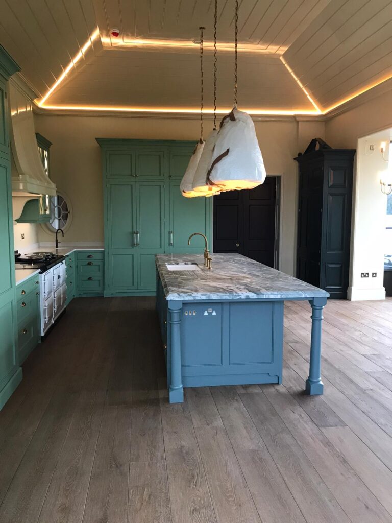 Kitchen with green painted cabinetry, a blue island topped with stone, brass taps and hanging pendant lights