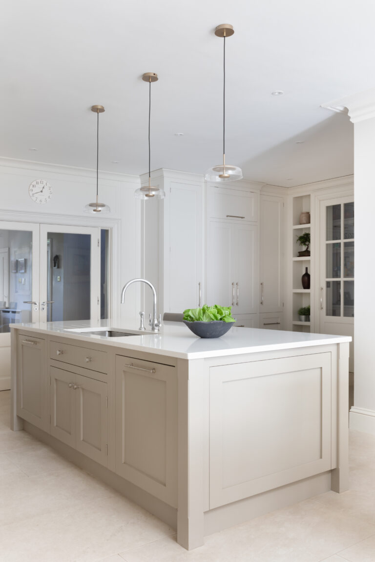 Large kitchen island with sink, chrome tap and three glass pendant lights above a white worktop